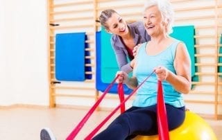 Physical Therapist happily helping a female patient use a stretch band