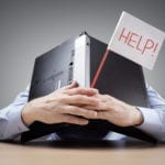 Businessman burying his head uner a laptop asking for help Struggling with Clean Claims